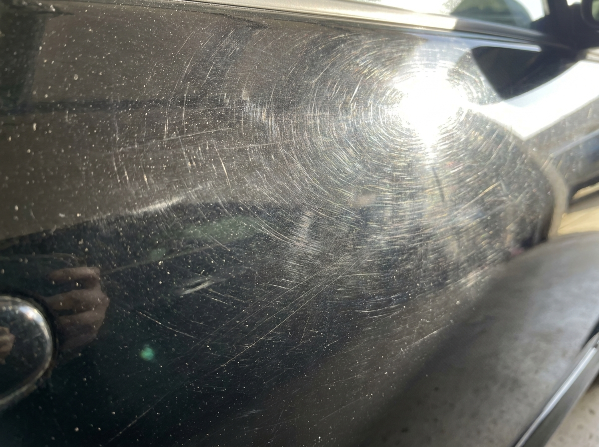 Close-up of black car paint with heavy swirl marks and scratches
